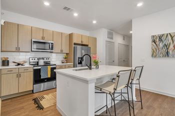 A kitchen with a large island with a white counter top and chairs